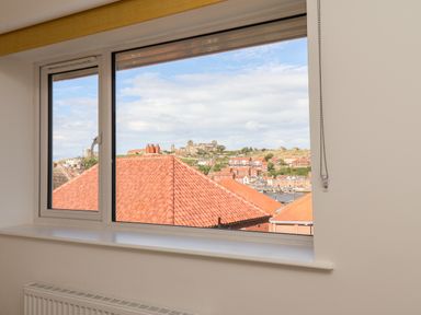 A window with tiled rooftops and a hillside town visible at Whitby View in Whitby