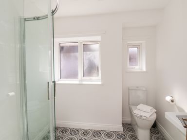 A bathroom with a shower door toilet with folded towels on top patterned floor tiles and frosted windows at Whitby View in Whitby