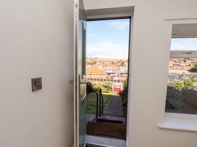 An open door showing a garden path leading to a red gate with a view of a town and hills at Whitby View in Whitby
