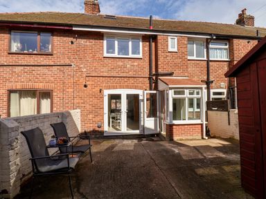 A rear view of a brick house with two black chairs on a concrete patio and an open door at Whitby View in Whitby