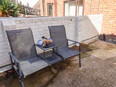Two black mesh chairs with a small table holding mugs, a French press, croissants, and grapes outside a brick house at Whitby View in Whitby