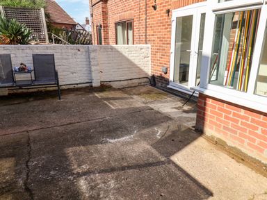 An outdoor patio area with concrete flooring a white brick wall two patio chairs and a small table with cups and fruit at Whitby View in Whitby