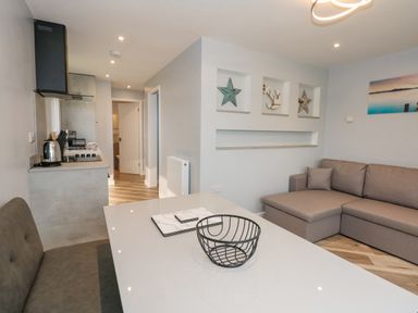 A living area with a gray sofa and a table with a wire basket and placemats in a kitchen space at Number 9 California Norfolk