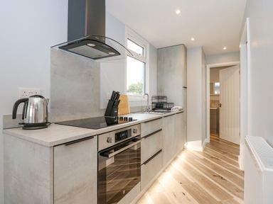 A narrow kitchen with a countertop electric stove oven sink and cabinets at Number 9 in California Norfolk