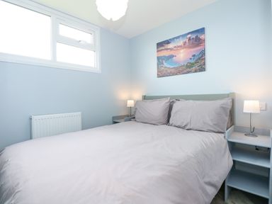 A bedroom with a double bed, bedside tables with lamps, a window, a radiator, and a landscape picture on the wall at Number 9 California Norfolk