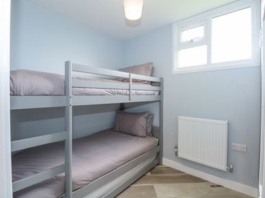 A small bedroom with a bunk bed with gray bedding and a window on the wall at Number 9 in California Norfolk