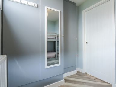 A room corner with a gray wardrobe featuring a full-length mirror reflecting bunk beds and a white door on the right at Number 9 California Norfolk