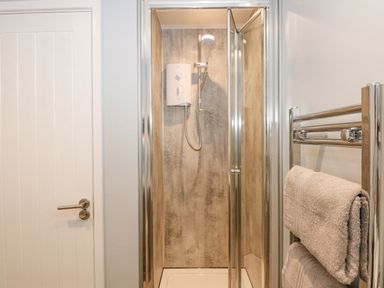 A shower cubicle with glass doors and a mounted shower heater next to a towel rack with folded towels in a bathroom at Number 9 in California Norfolk