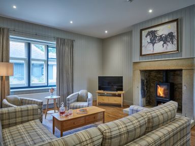 A living room with plaid sofas and armchairs a coffee table and a fireplace with a horse painting above at The Filly in Humshaugh