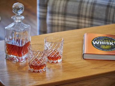 A wooden table with a glass decanter and two glasses containing whisky and a book about whisky on the side at The Filly in Humshaugh