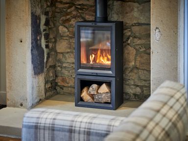 A wood burning stove with fire and logs inside a stone fireplace at The Filly in Humshaugh