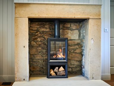A stone fireplace with a metal wood-burning stove and logs inside at The Filly in Humshaugh