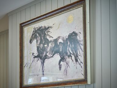 A framed painting of a black horse on a paneled wall at The Filly in Humshaugh