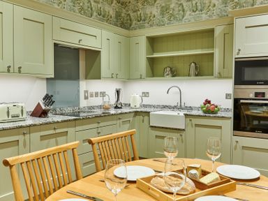 A kitchen with green cabinets a granite countertop a sink a toaster an oven and a dining table with plates glasses and bread at The Filly in Humshaugh