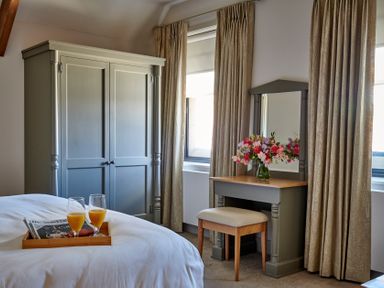 A bedroom with a bed tray holding two glasses of orange juice and newspapers a gray wardrobe a dressing table with a vase of flowers and a stool at The Filly in Humshaugh