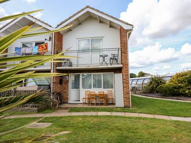 A two story house with a balcony and outdoor chairs and table at 63 The Waterside Holiday Park in Corton