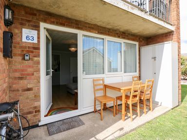 An outdoor patio area with a wooden table and four chairs next to a glass door at 63 The Waterside Holiday Park in Corton