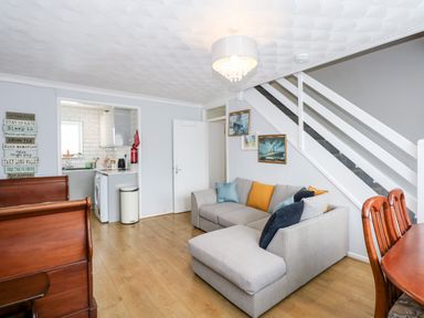 A living room with a gray corner sofa with cushions under stairs and a kitchen visible through a doorway at 63 The Waterside Holiday Park in Corton