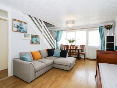 A living room with a gray sectional sofa orange and blue cushions wooden dining table with chairs and teal curtains at 63 The Waterside Holiday Park in Corton