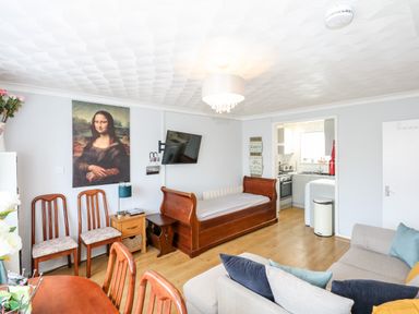 A living room with wooden chairs a small wooden table a television a wooden daybed a sofa and a kitchen area at 63 The Waterside Holiday Park in Corton
