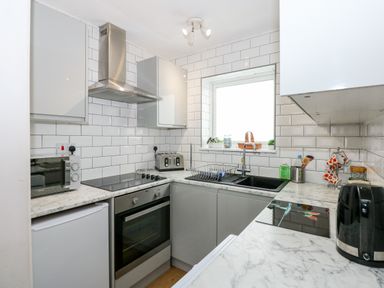 A kitchen with white tiled walls gray cabinets marble countertops a black sink a toaster a microwave an oven and a window at 63 The Waterside Holiday Park in Corton