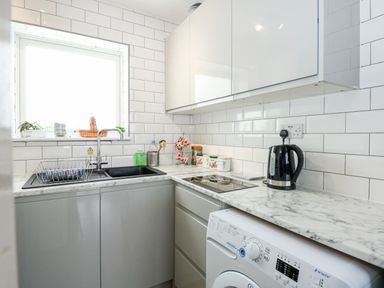 A small kitchen with a sink a dish rack countertop cabinets an electric kettle and a washing machine at 63 The Waterside Holiday Park in Corton