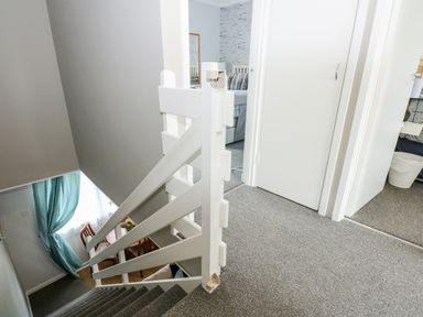A stairway with white wooden railing leading down to a dining area with blue curtains and a small round table at 63 The Waterside Holiday Park in Corton