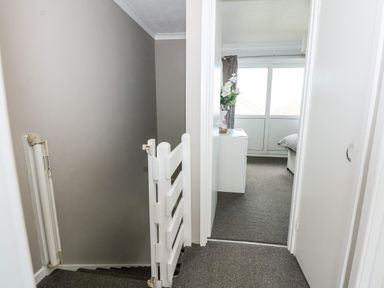 A hallway with stairs and a baby gate leading to a bedroom with a dresser and window at 63 The Waterside Holiday Park in Corton
