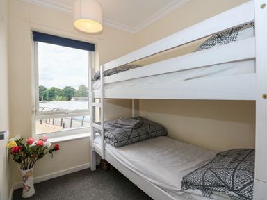 A bedroom with a white bunk bed next to a window and a vase of flowers on the floor at 63 The Waterside Holiday Park in Corton