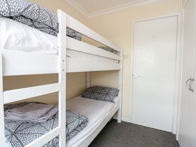 A bedroom with a white bunk bed gray patterned bedding and towels on a carpeted floor at 63 The Waterside Holiday Park in Corton