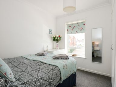 A bedroom with a bed next to a window with floral blinds and a chest of drawers with flowers at 63 The Waterside Holiday Park in Corton