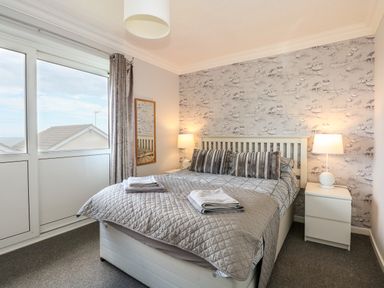 A bedroom with a bed two bedside tables with lamps a wall mirror and a large window at 63 The Waterside Holiday Park in Corton
