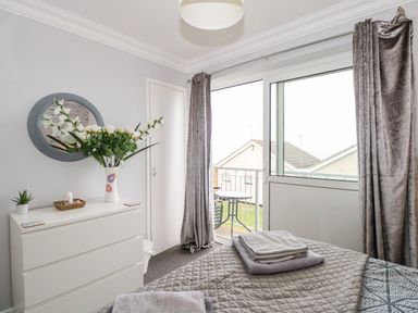 A bedroom with a bed folded towels on a chest of drawers flowers in a vase a round mirror and sliding glass door leading to a balcony at 63 The Waterside Holiday Park in Corton