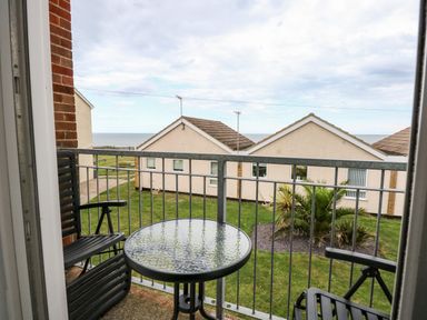 A balcony with a round glass table and two black chairs overlooking houses gardens and the sea at 63 The Waterside Holiday Park in Corton