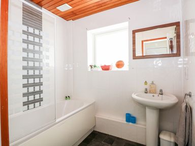 A bathroom with a bathtub shower, a pedestal sink, mirror, window, and towels at 63 The Waterside Holiday Park in Corton