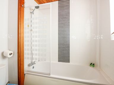 A bathroom with a bathtub shower combination and a wall-mounted toilet paper holder at 63 The Waterside Holiday Park in Corton