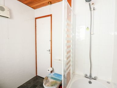 A bathroom with a toilet featuring a beach-themed seat cover a shower with a glass screen and a wooden ceiling at 63 The Waterside Holiday Park in Corton