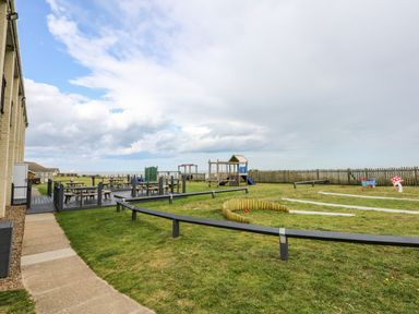 An outdoor playground and picnic area with wooden benches and play structures at 63 The Waterside Holiday Park in Corton