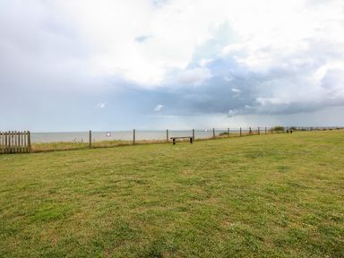 A grassy area with a wooden bench and a fence along the coastline at 63 The Waterside Holiday Park in Corton