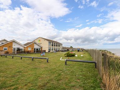 An outdoor mini golf course with buildings in the background and a fenced shoreline at 63 The Waterside Holiday Park in Corton