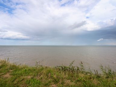 A grassy shoreline overlooking a calm sea with a cloudy sky at 63 The Waterside Holiday Park in Corton