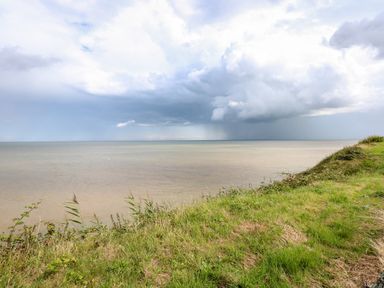 A grassy seaside cliff overlooking the ocean under a cloudy sky at 63 The Waterside Holiday Park in Corton