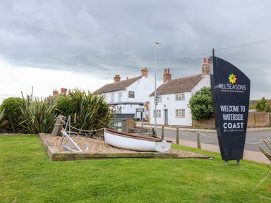An outdoor display with a white boat and anchor on gravel next to a sign for Allseasons Waterside Coast Bar and Restaurant in front of houses