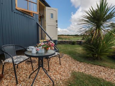 A small outdoor seating area with a table and two chairs outside a building with open door and window at Dot May Porteath near Polzeath
