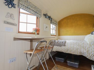 A small bedroom with a bed a table with two chairs two windows and a yellow accent wall at Dot May Porteath near Polzeath