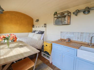 A kitchen and dining area with a table and flowers a bed and kitchen cabinets at Dot May Porteath near Polzeath