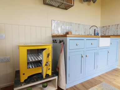 A kitchen with blue cabinets a white sink a yellow appliance with an open door and a towel hanging at Dot May Porteath near Polzeath