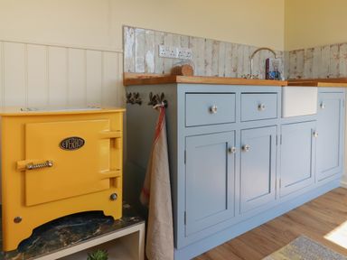 A kitchen with a yellow Everhot stove blue cabinets a wooden countertop a white sink and a cookbook at Dot May Porteath near Polzeath