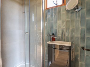 A bathroom with a glass shower enclosure a small sink with cabinet and a green tiled wall at Dot May Porteath near Polzeath