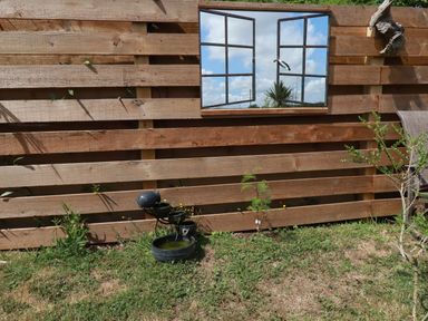 A wooden fence with a mirror reflecting the sky and clouds and a water feature on grass at Dot May in Porteath near Polzeath